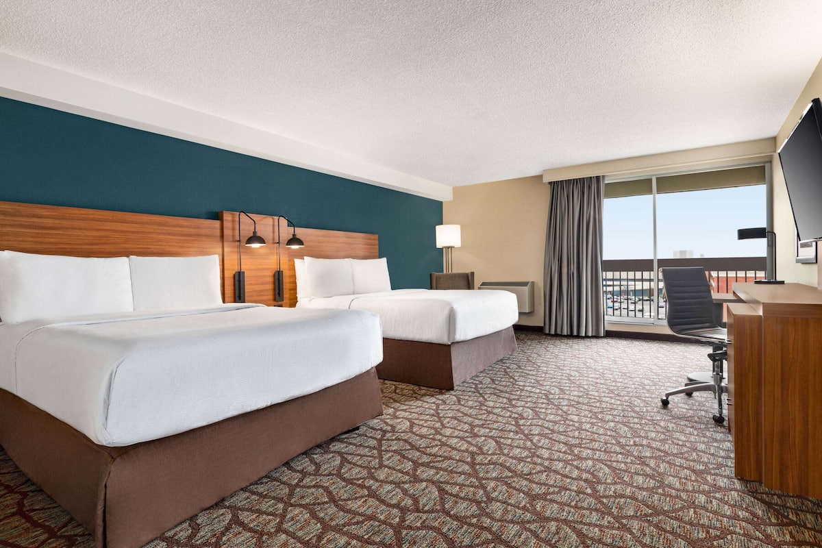 Une chambre d’hôtel avec deux lits, un bureau, une chaise, une télévision et un balcon avec vue.