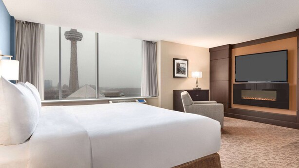 Habitación de hotel con una cama grande, televisión, chimenea y vista a una torre por la ventana.
