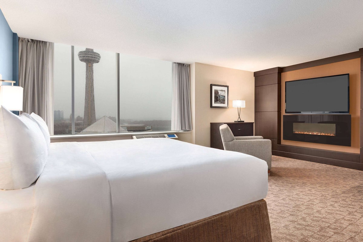 Une chambre d’hôtel avec un grand lit, une télévision, une cheminée et une vue sur une tour depuis la fenêtre.