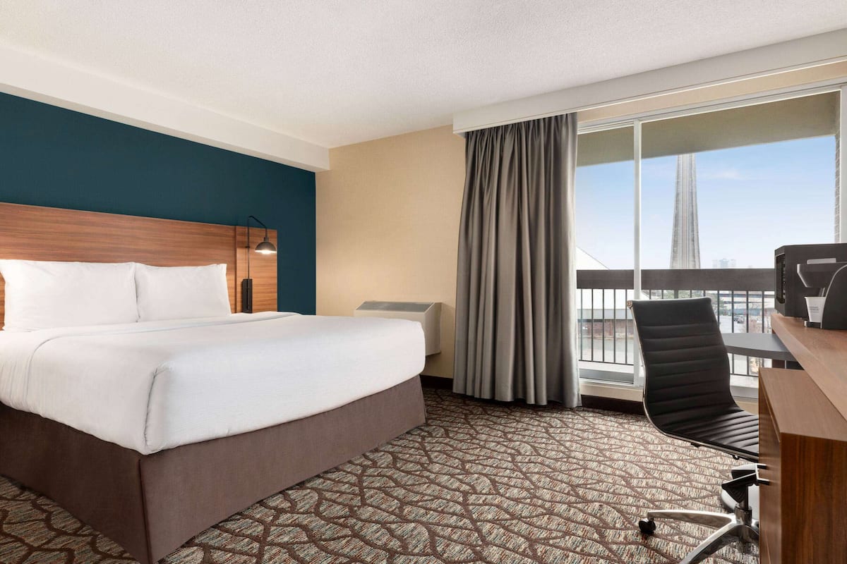 Une chambre d’hôtel avec un grand lit, un bureau, une chaise, une fenêtre donnant sur un pont et une moquette à motifs.