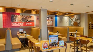Un interior de restaurante moderno con cabinas y mesas, un atril para el menú e imágenes promocionales en una pared.