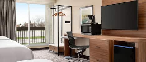Una habitación de hotel con una cama grande, un escritorio con computadora, un televisor de pantalla plana y un ventanal corredizo al exterior.
