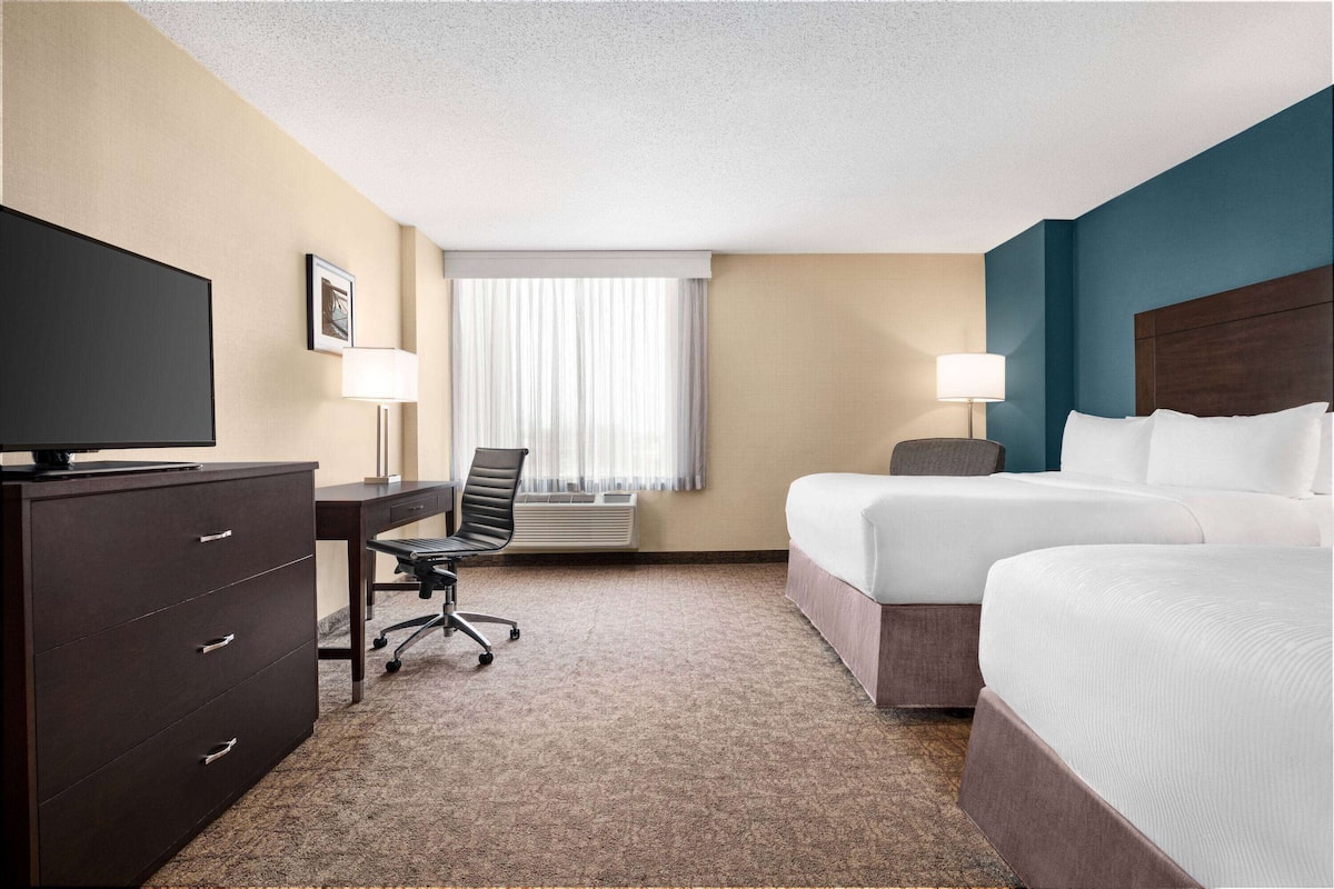 Une chambre d’hôtel équipée d’un lit, d’un bureau, d’une chaise, d’une télévision et d’une fenêtre avec des rideaux.
