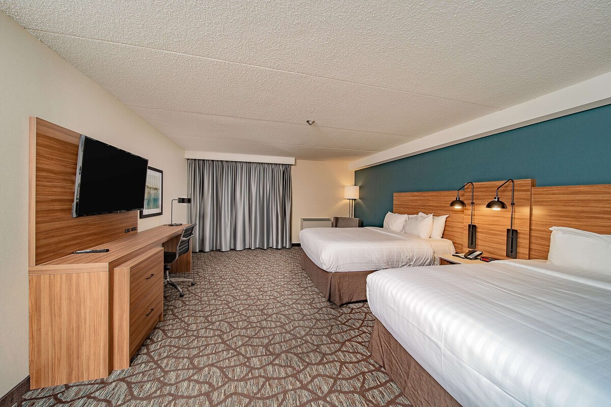 Ein Hotelzimmer mit einem Holztisch, einem Flachbildfernseher, zwei Betten, einem gemusterten Teppich und einer blauen Akzentwand.