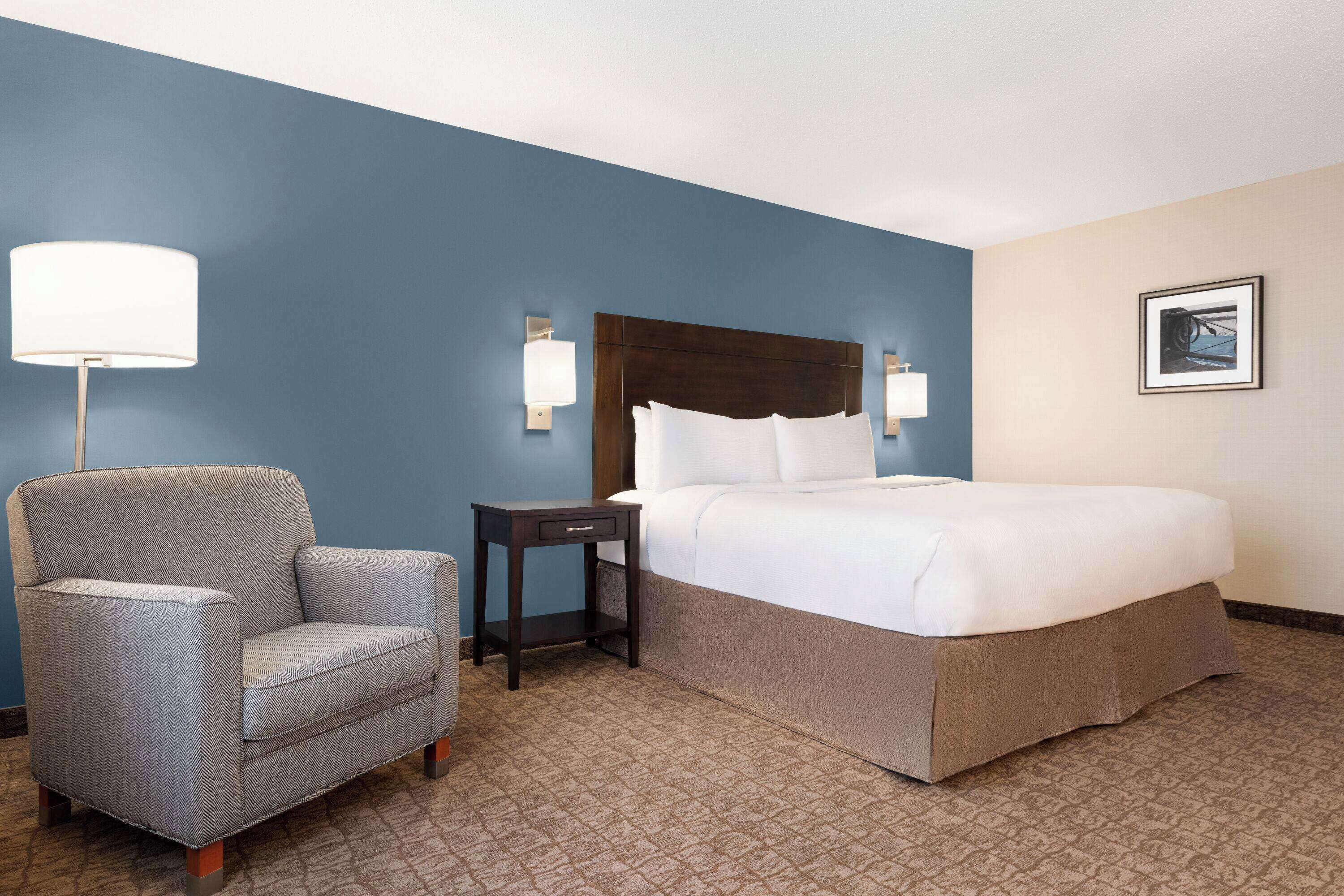 Une chambre d’hôtel avec un lit, une chaise, une table de chevet et une lampe.