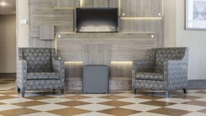 A lobby with two patterned armchairs, a small ottoman, and a flat-screen TV mounted on a wooden wall. - Comfort Inn Fallsview (Niagara Falls)