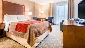 A hotel room with a large bed, a desk, two chairs, a TV, and a window with curtains. - Comfort Inn Fallsview (Niagara Falls)