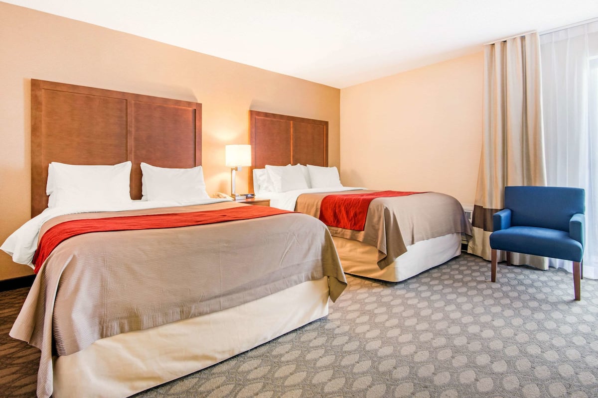 A hotel room with two beds, a desk, a chair, and a patterned carpet.