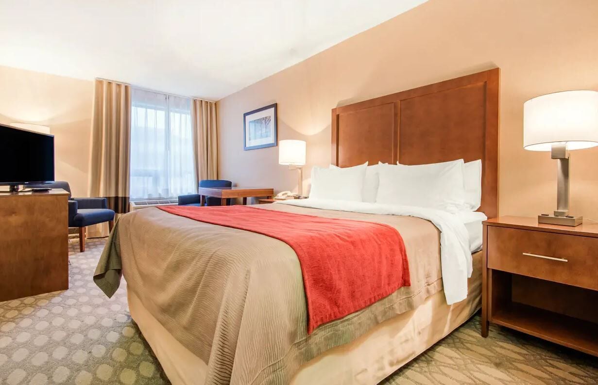 A hotel room with a bed, bedside tables, a desk, a chair, a TV, and a window with curtains.