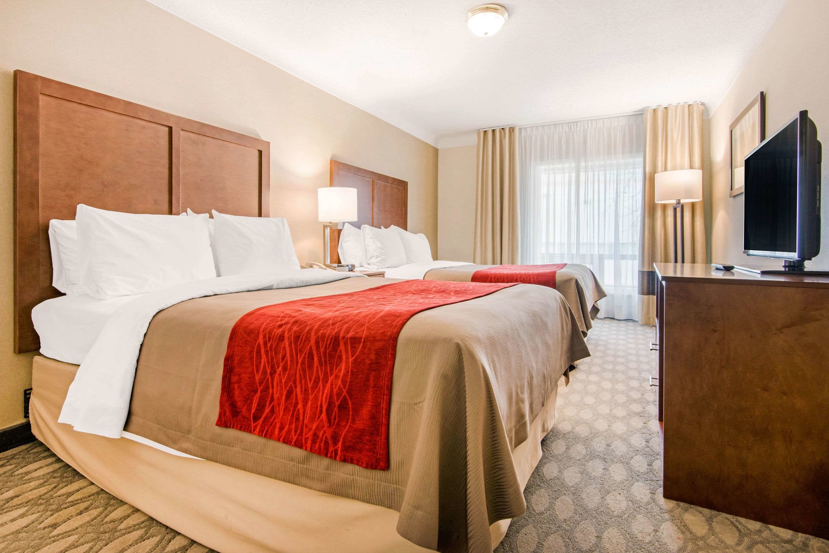A hotel room with two beds, a desk, a television, and a window with curtains.