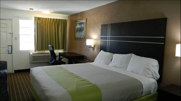 A hotel room with a large bed, a desk, a chair, a window with curtains, and a painting on the wall.