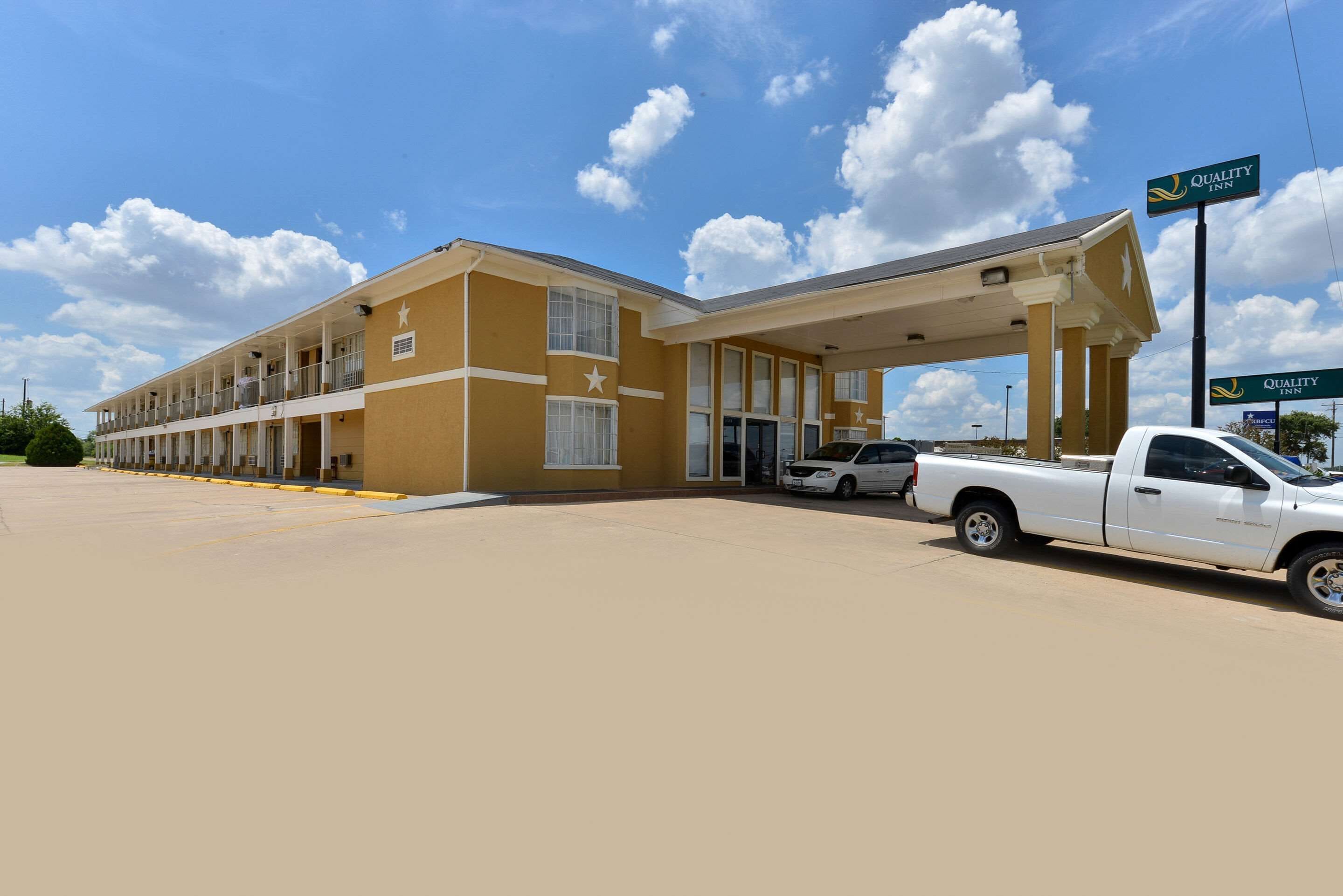 A motel with a two-story structure, a covered parking area, and a white pickup truck parked in front.