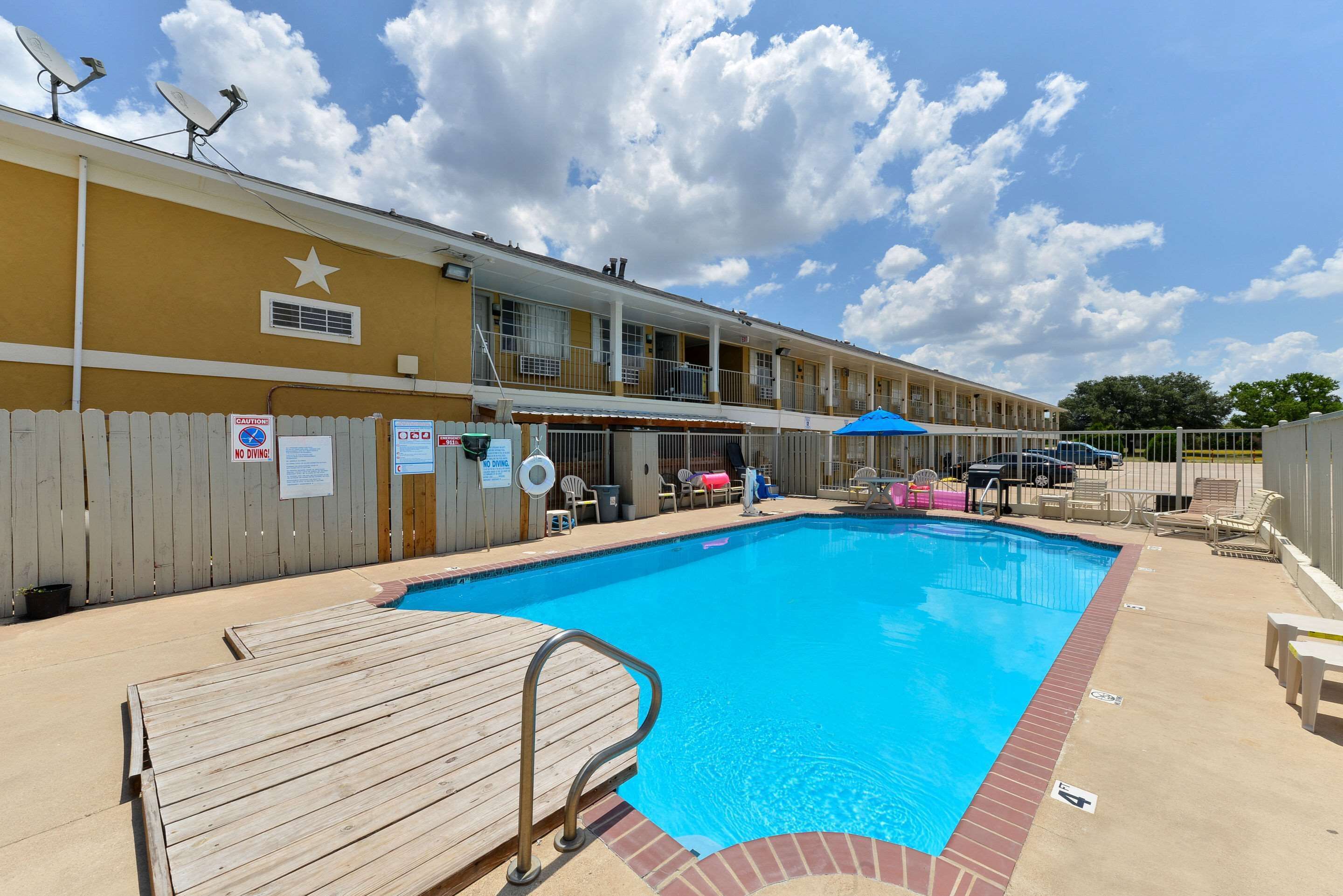 A hotel with a pool, wooden deck, and a fenced area.