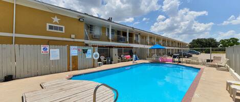 A hotel with a pool, wooden deck, and a fenced area.