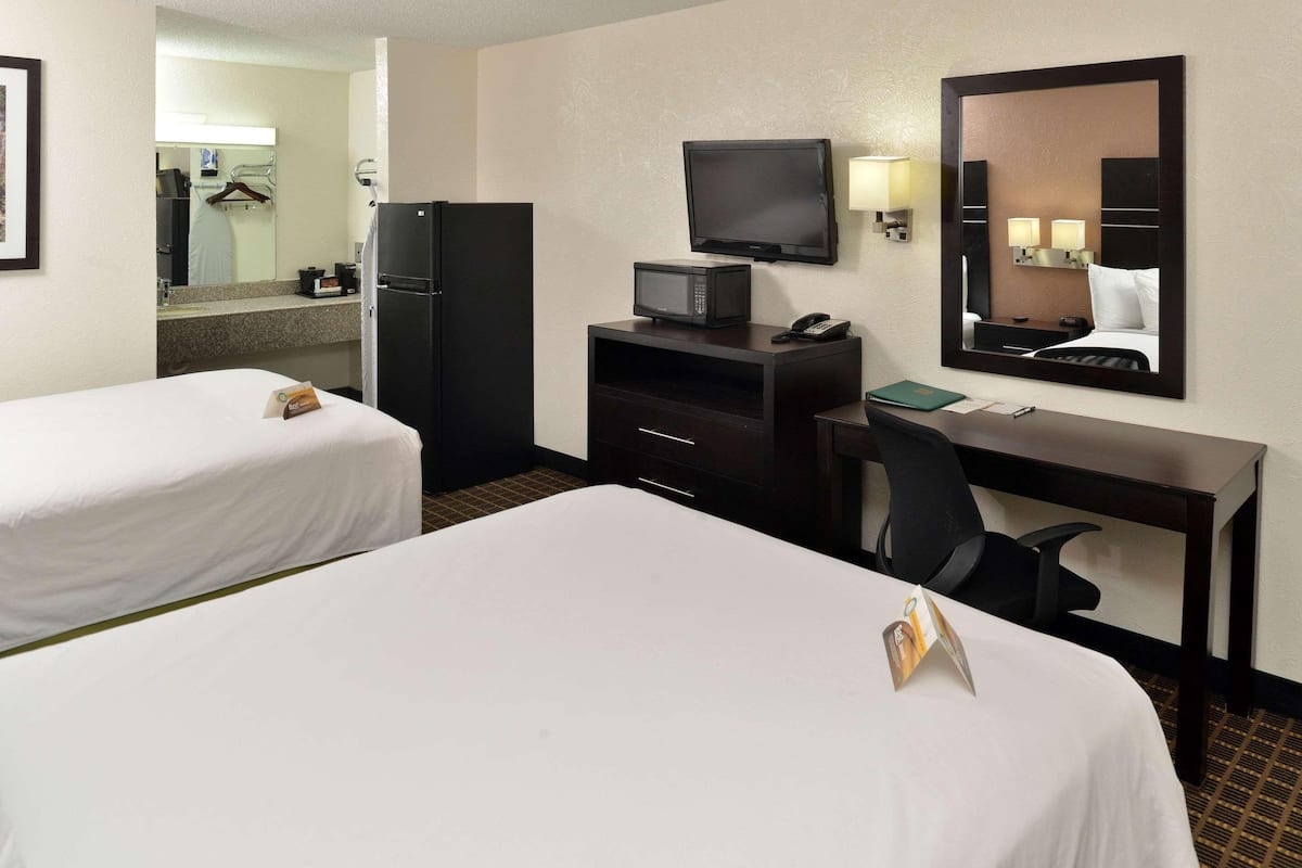 A hotel room with two beds, a desk, a television, a refrigerator, and a mirror.