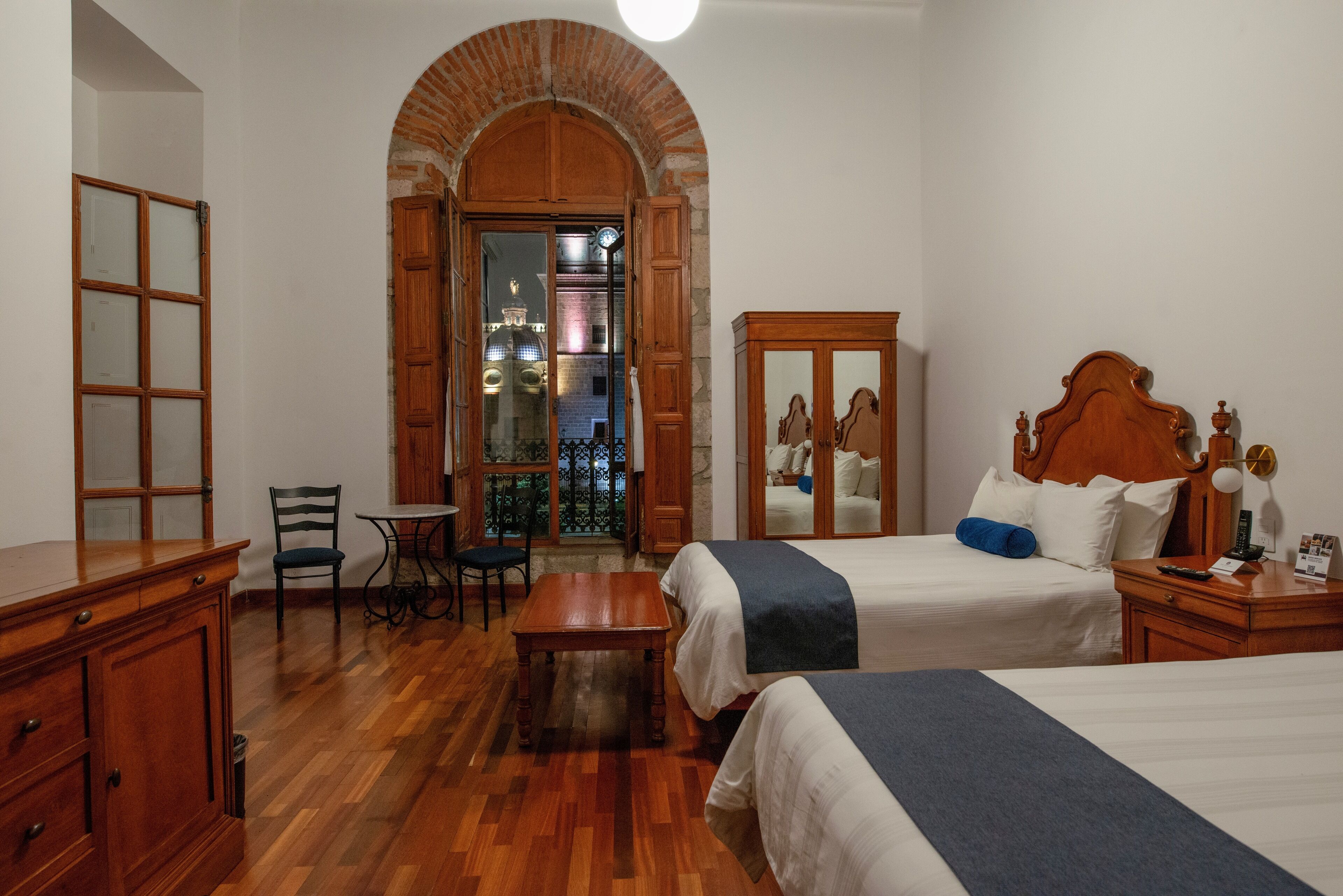 A hotel room with two beds, a wooden desk, a chair, and a small table.