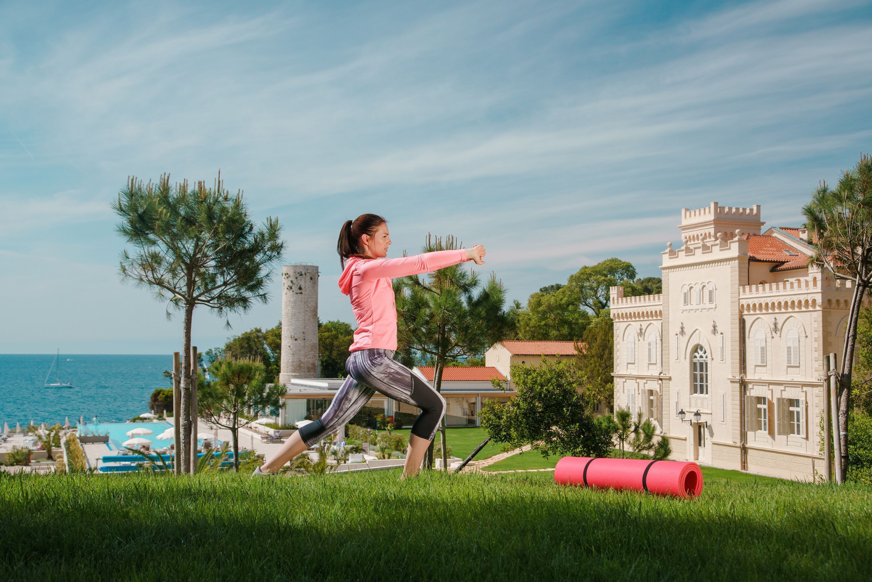 A person stretching outdoors with a building and a body of water in the background.