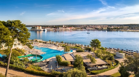 A resort with a large swimming pool, a water slide, and a view of the city across the water.
