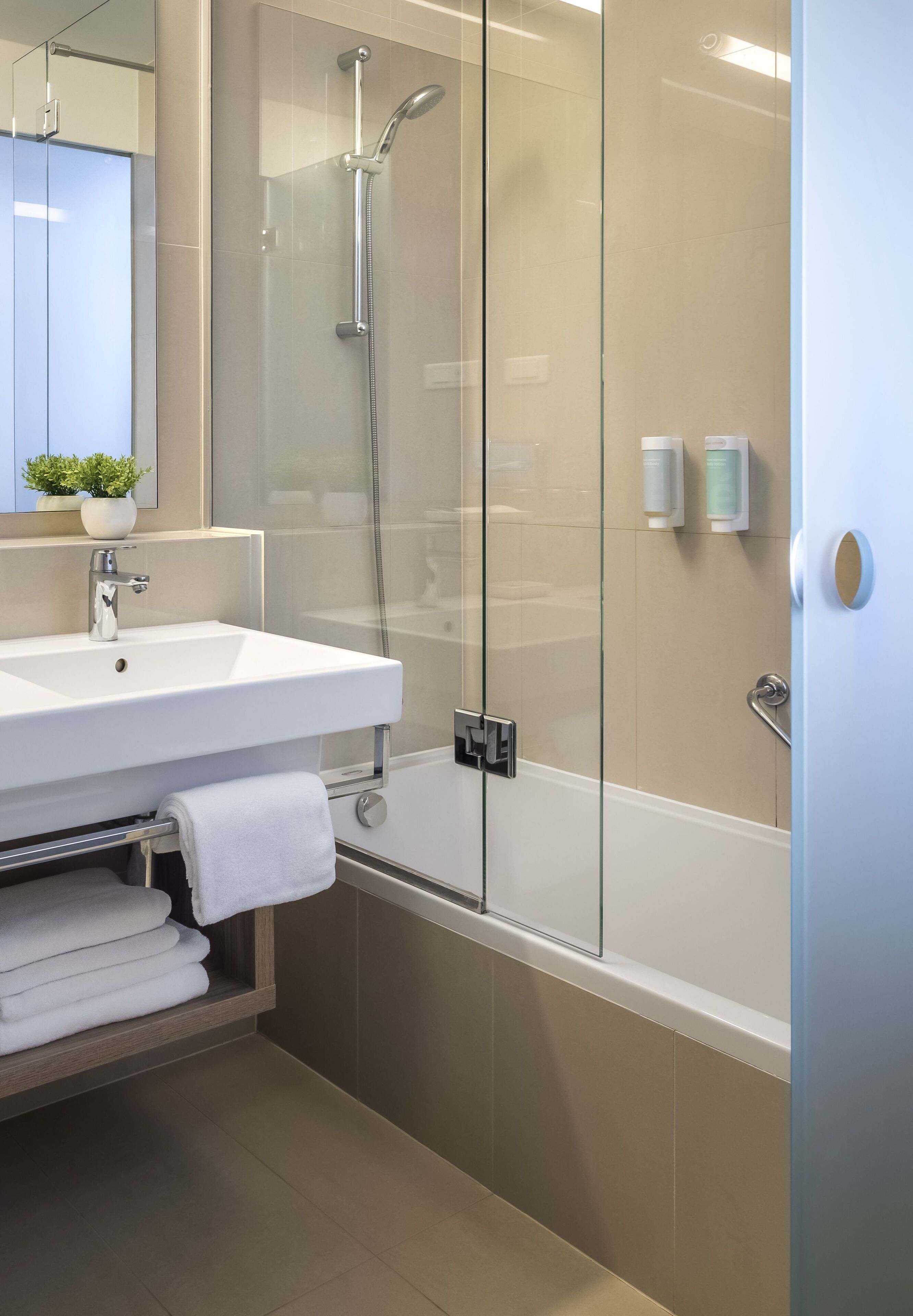Een moderne badkamer met een douchecabine van glas, een witte wastafel en een handdoekrek.