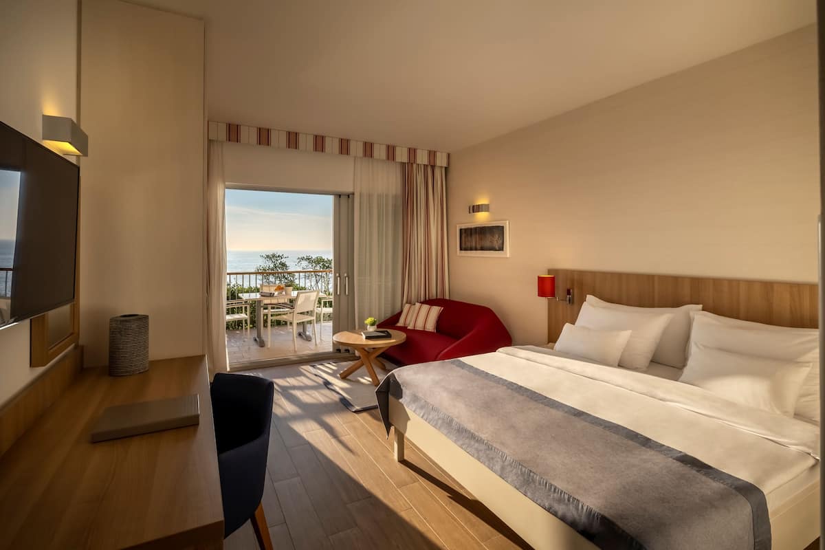 Una camera d'albergo con un letto grande, una scrivania con una sedia, una televisione e un balcone con mobili da esterno.