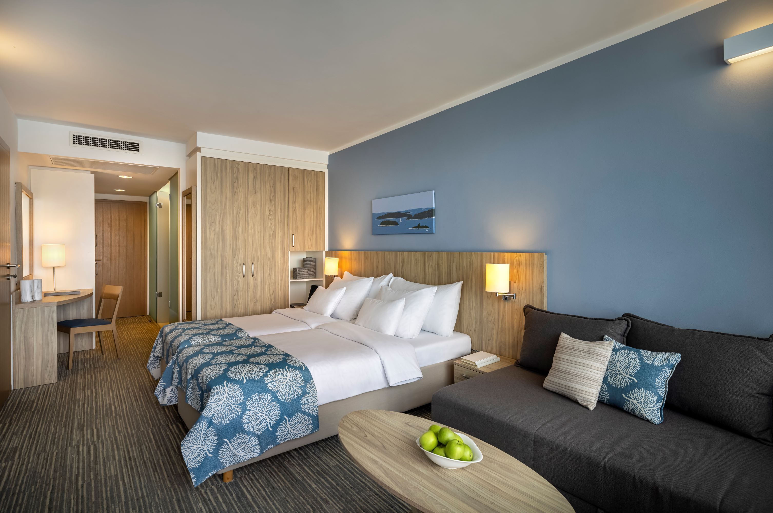 Una habitación de hotel con una cama, un sofá, un escritorio y un frutero.