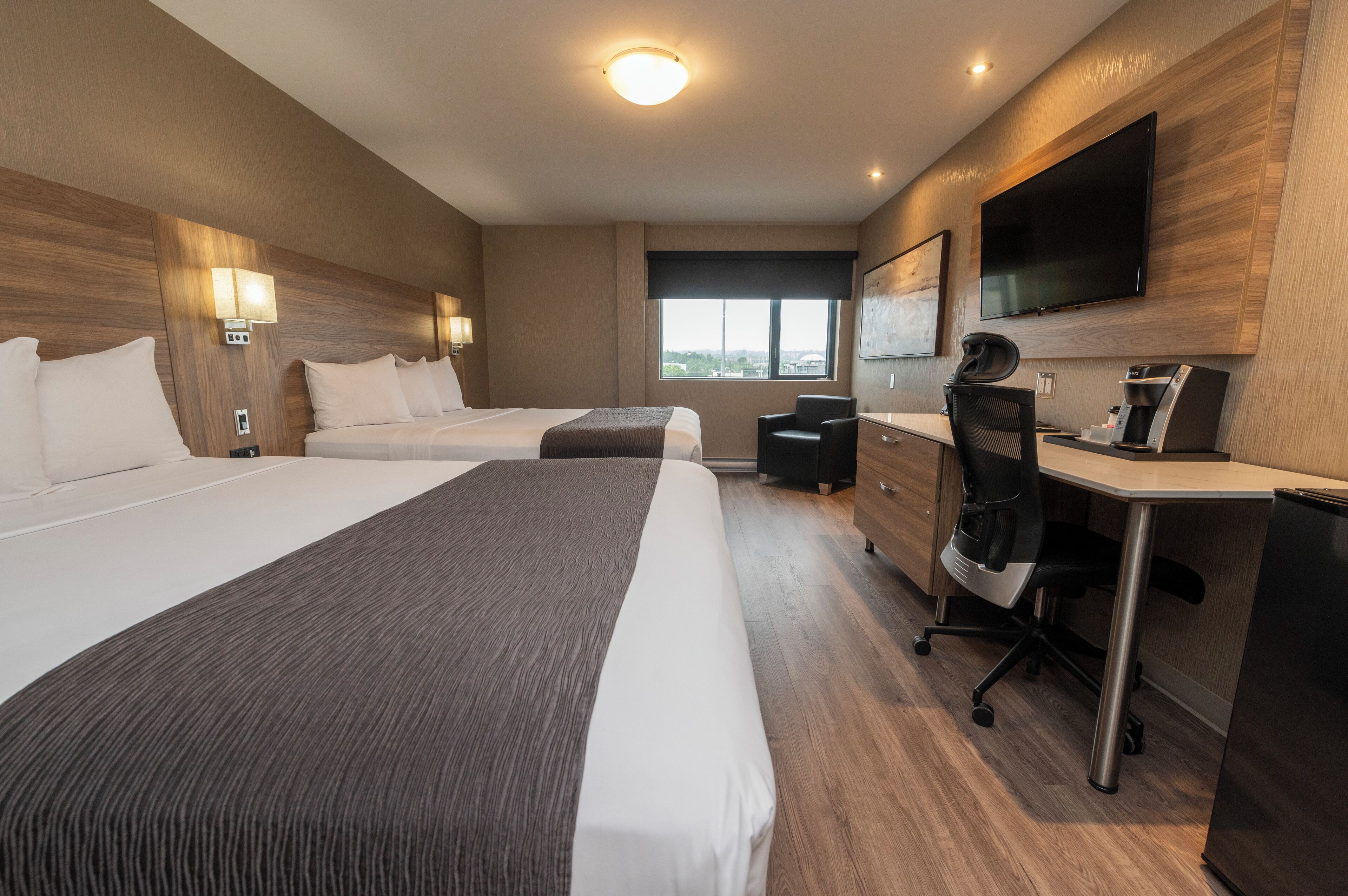Habitación de hotel con dos camas, un escritorio, una silla, un televisor de pantalla plana y una ventana.