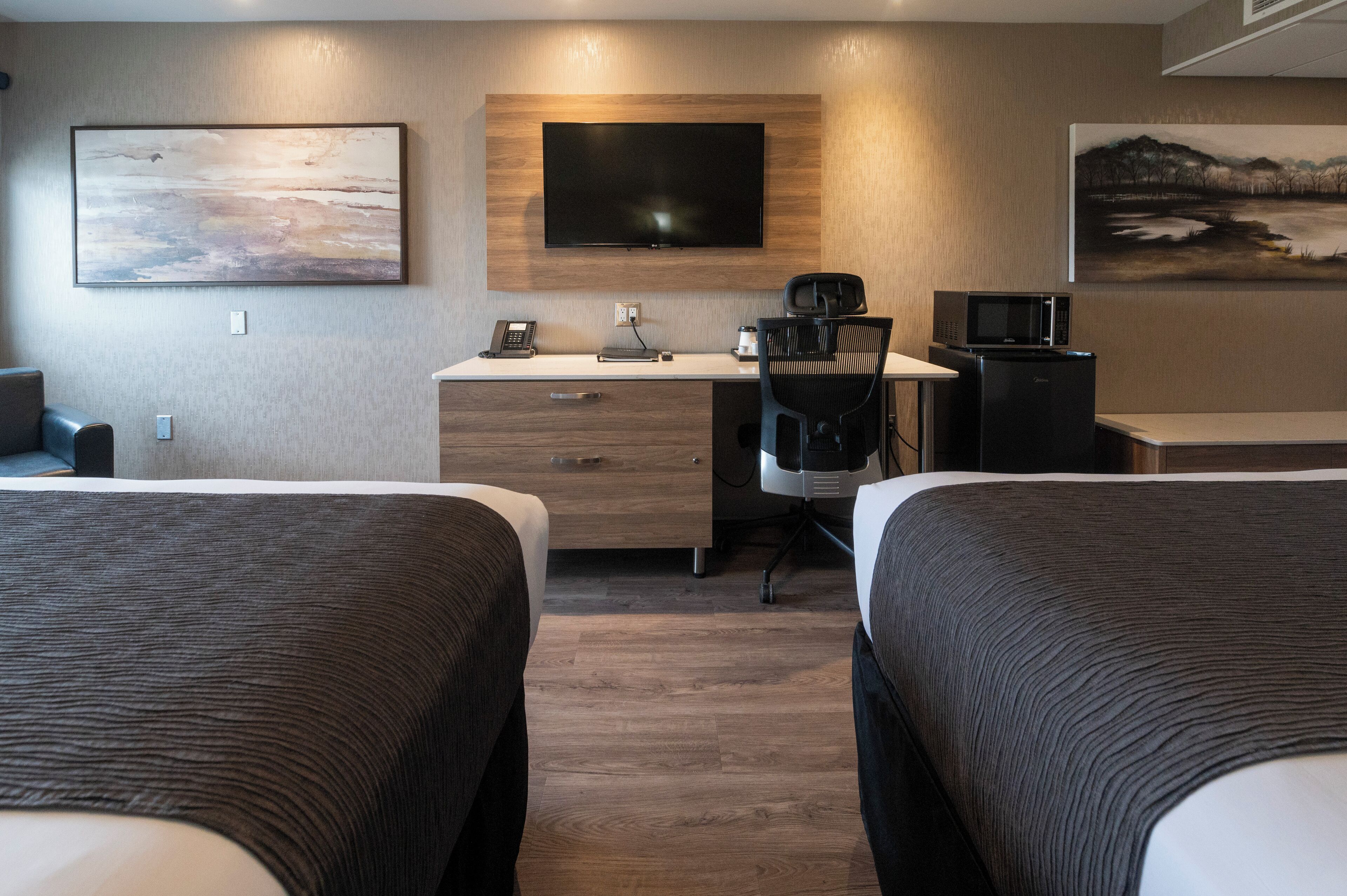 Ett hotellrum med två sängar, ett skrivbord med en dator, en stol, en tv och en mikrovågsugn.