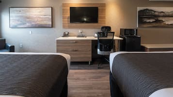 Ett hotellrum med två sängar, ett skrivbord med en dator, en stol, en tv och en mikrovågsugn.