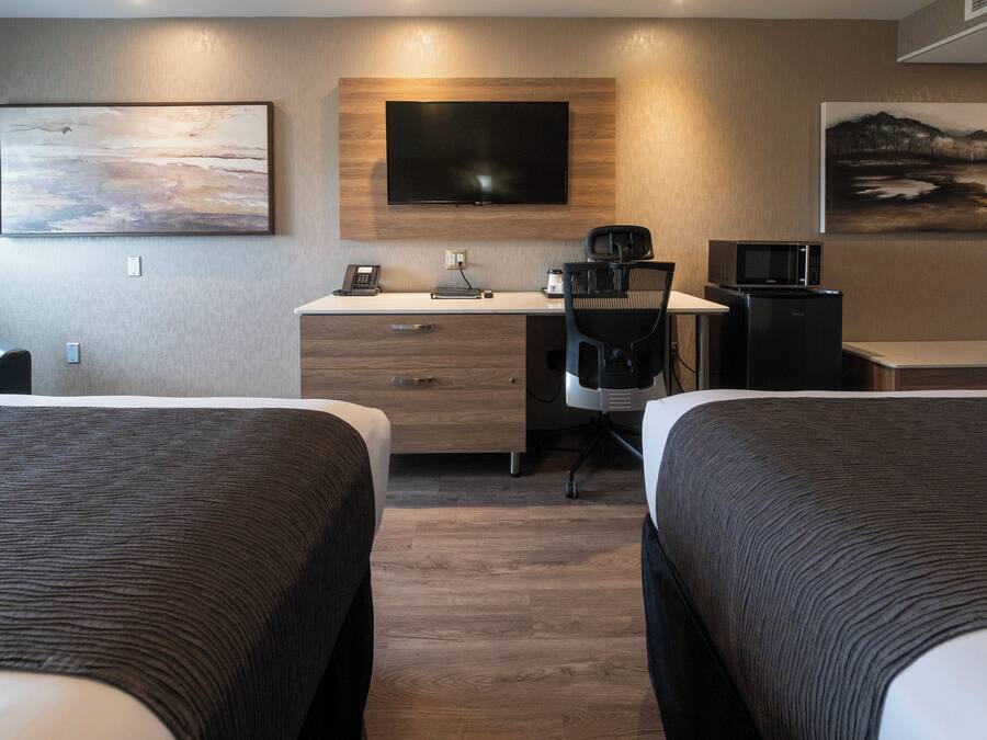 Ett hotellrum med två sängar, ett skrivbord med en dator, en stol, en tv och en mikrovågsugn.