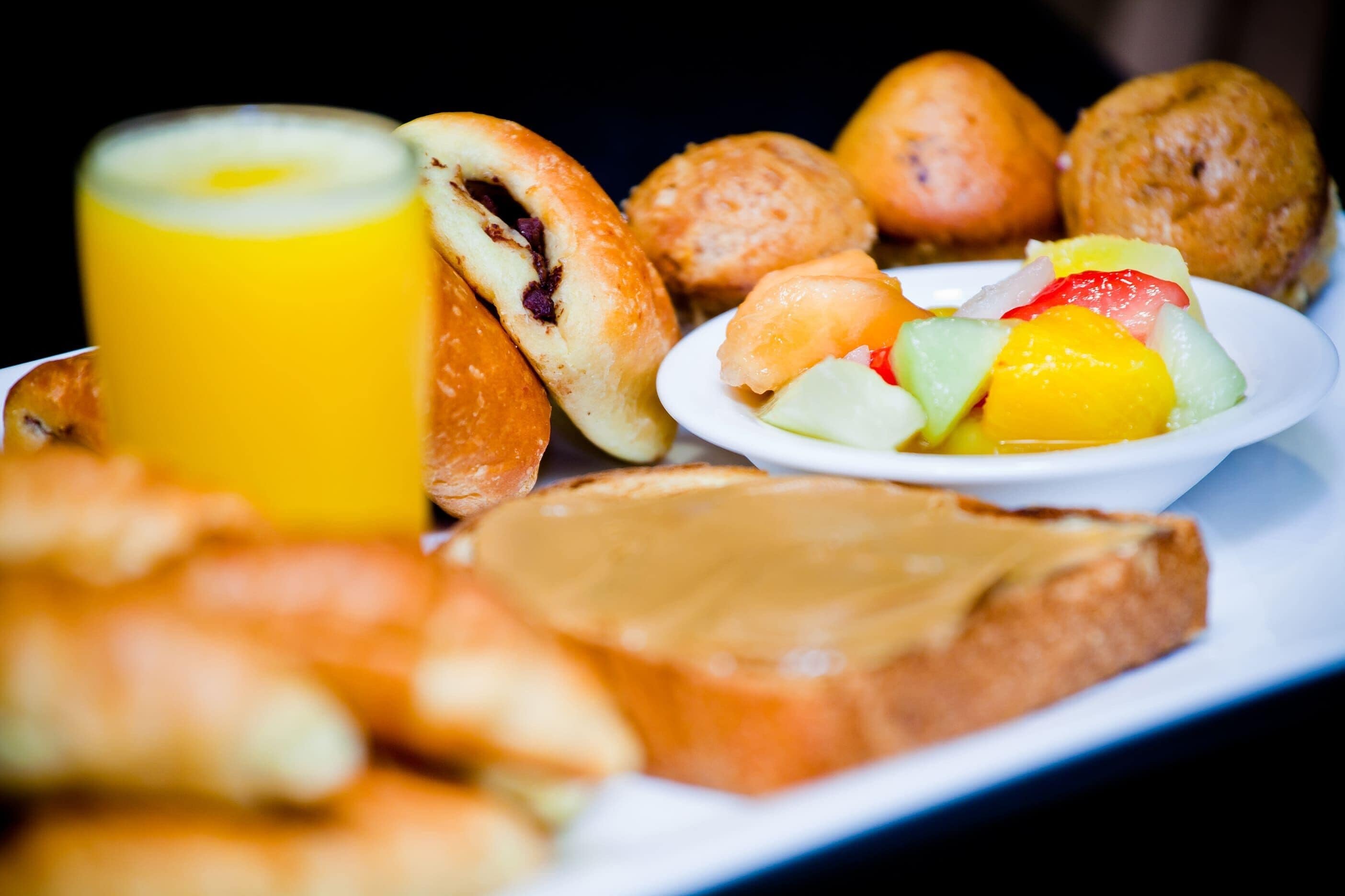 Bandeja de desayuno con pasteles, un vaso de jugo de naranja y una fuente de fruta.