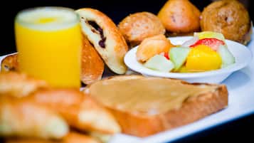 Bandeja de desayuno con pasteles, un vaso de jugo de naranja y una fuente de fruta.