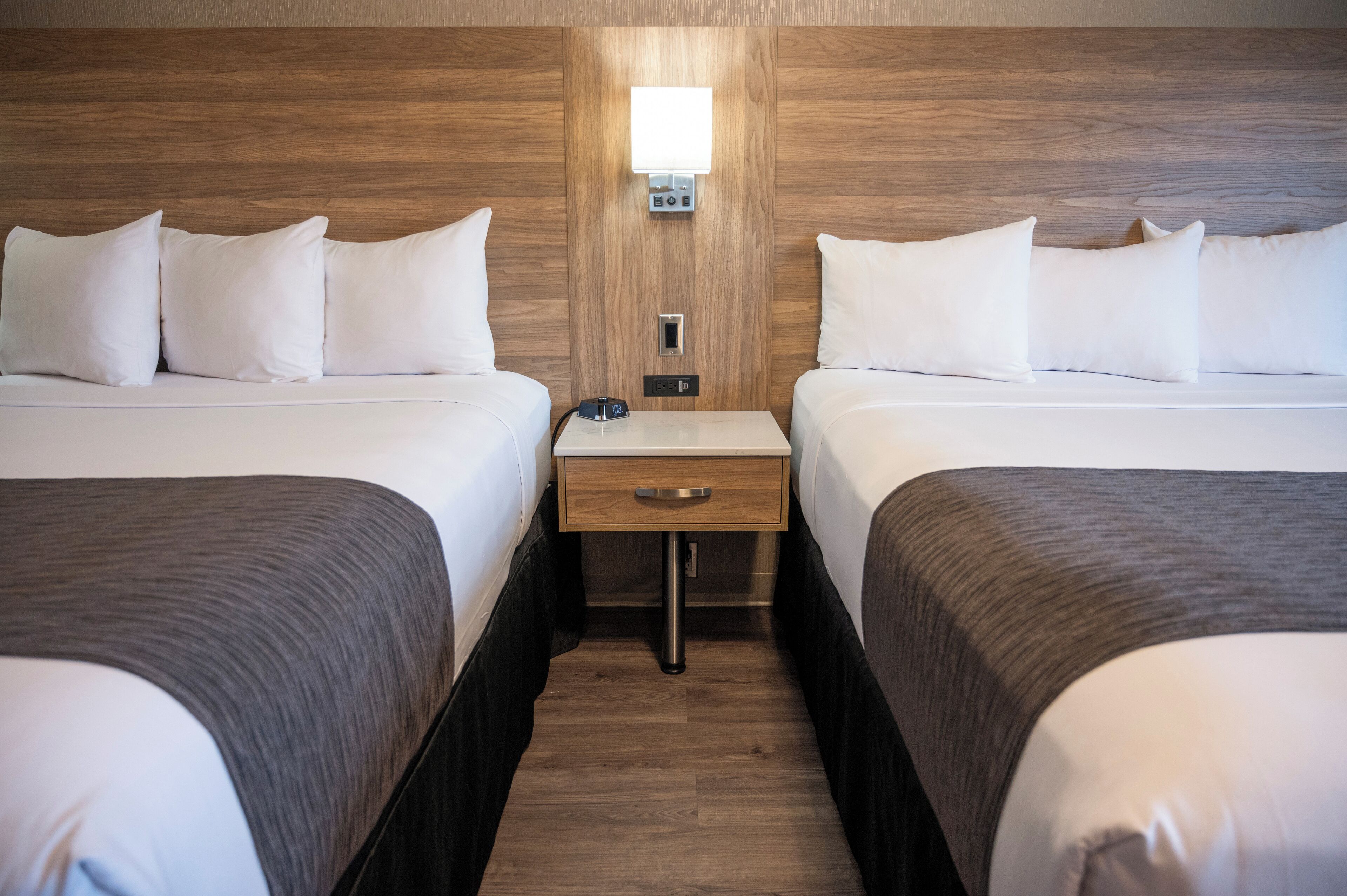A hotel room with two beds, a nightstand, a lamp, and a wooden headboard.