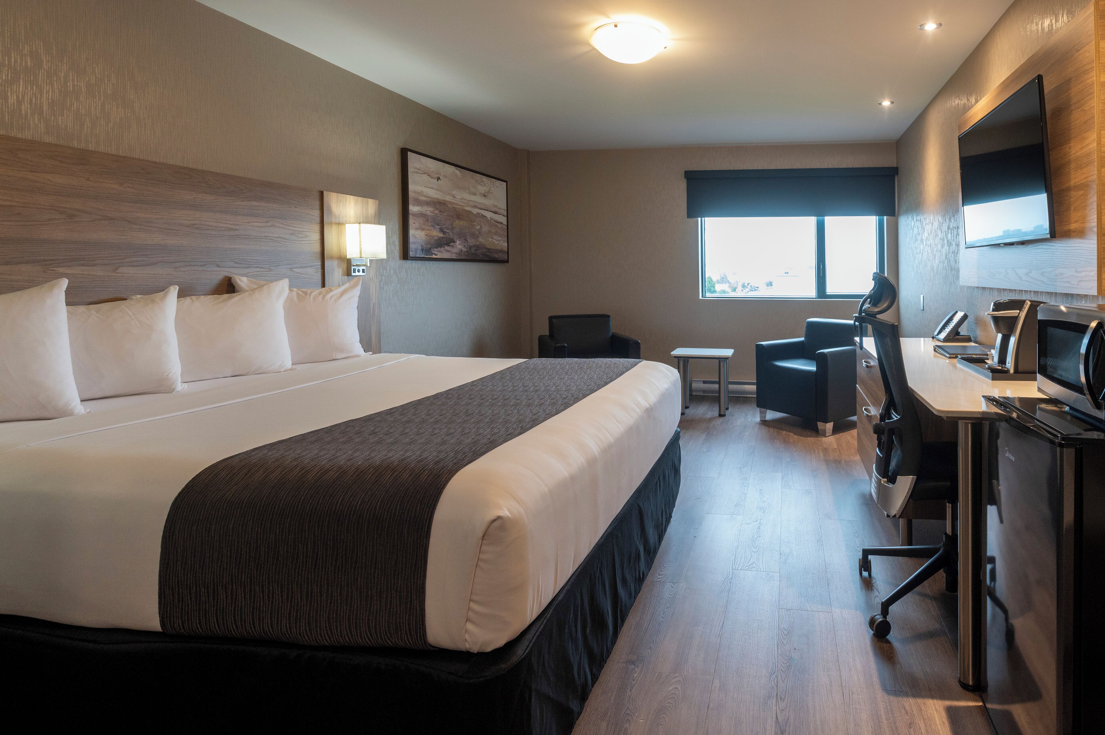 Una habitación de hotel moderna con una cama grande, un escritorio con computadora, una silla y un televisor.