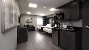 A modern hotel room with a kitchenette, a sofa, a bed, and a large window.