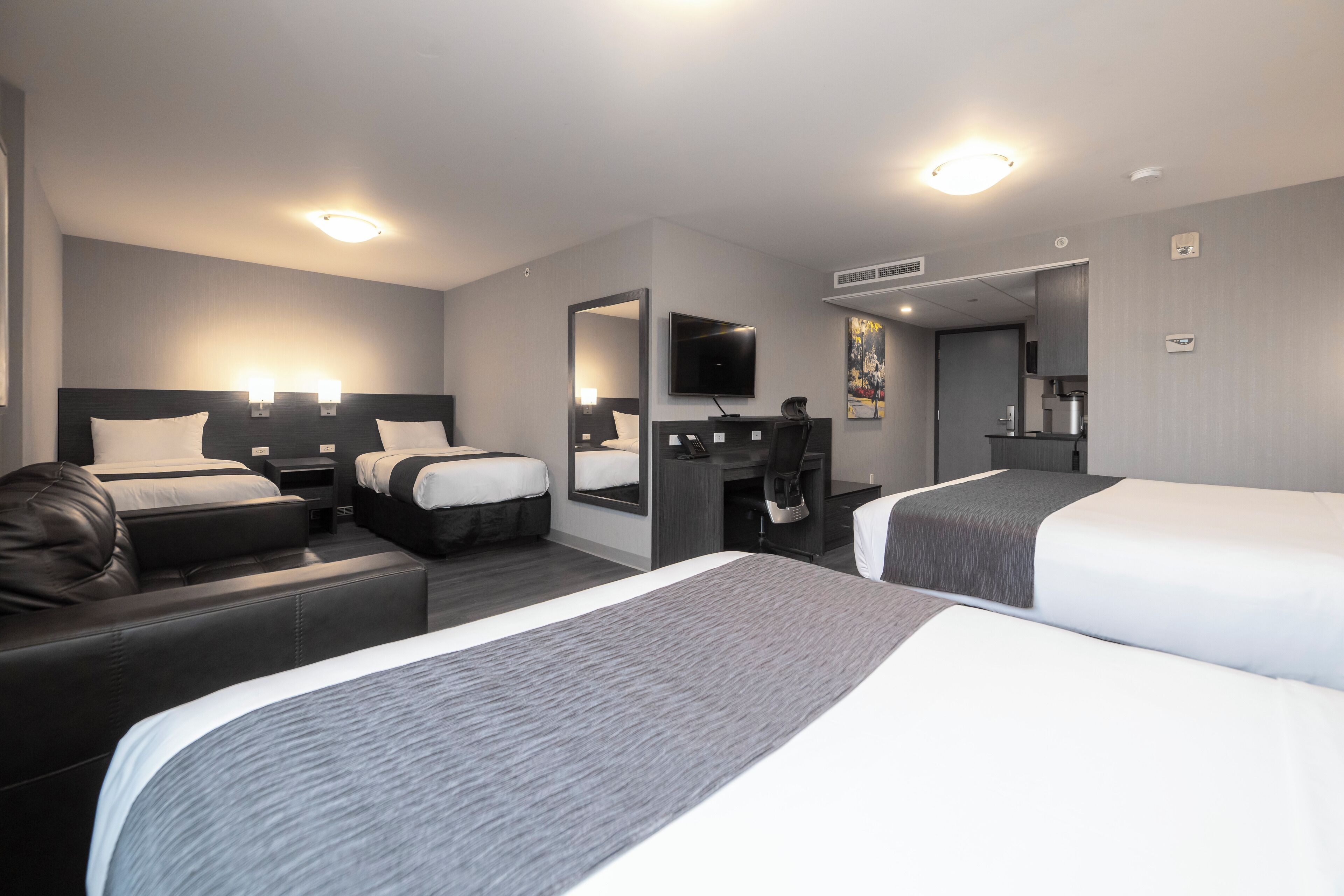 Une chambre d’hôtel avec deux lits, un canapé, un bureau, une télévision et un miroir.