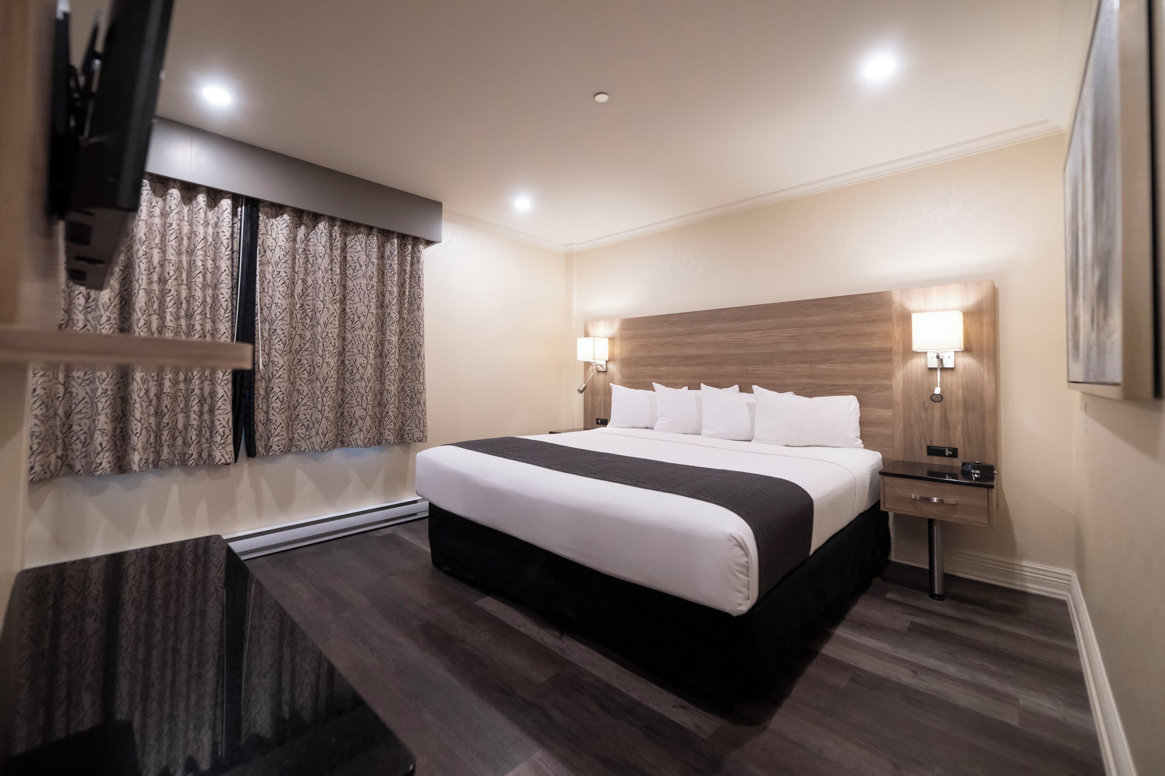 Habitación de hotel con una cama grande, lámparas de noche, un televisor de pantalla plana y un ventanal con cortinas.
