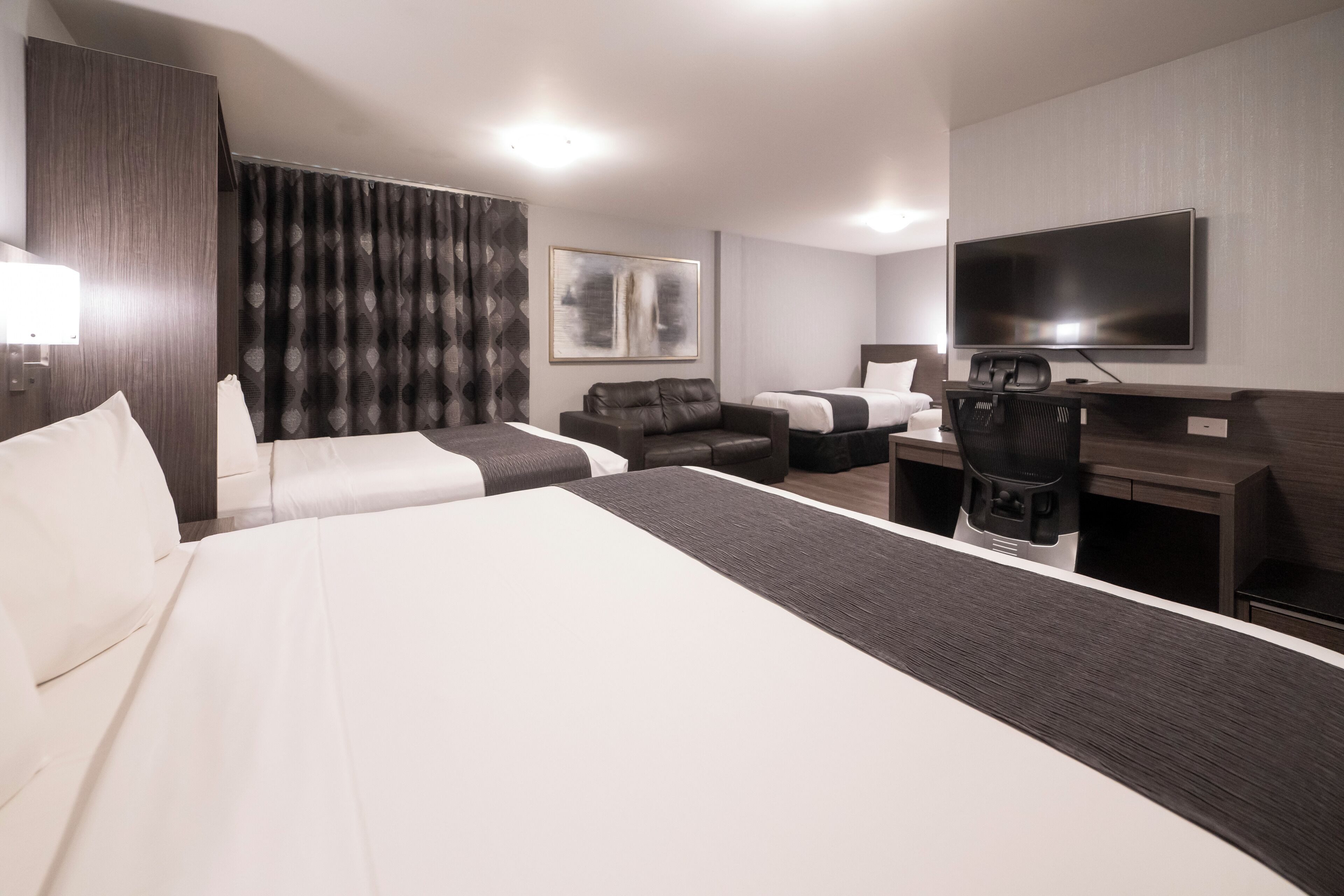 Una habitación de hotel moderna con una cama grande, un escritorio, una silla, un televisor y un sofá.