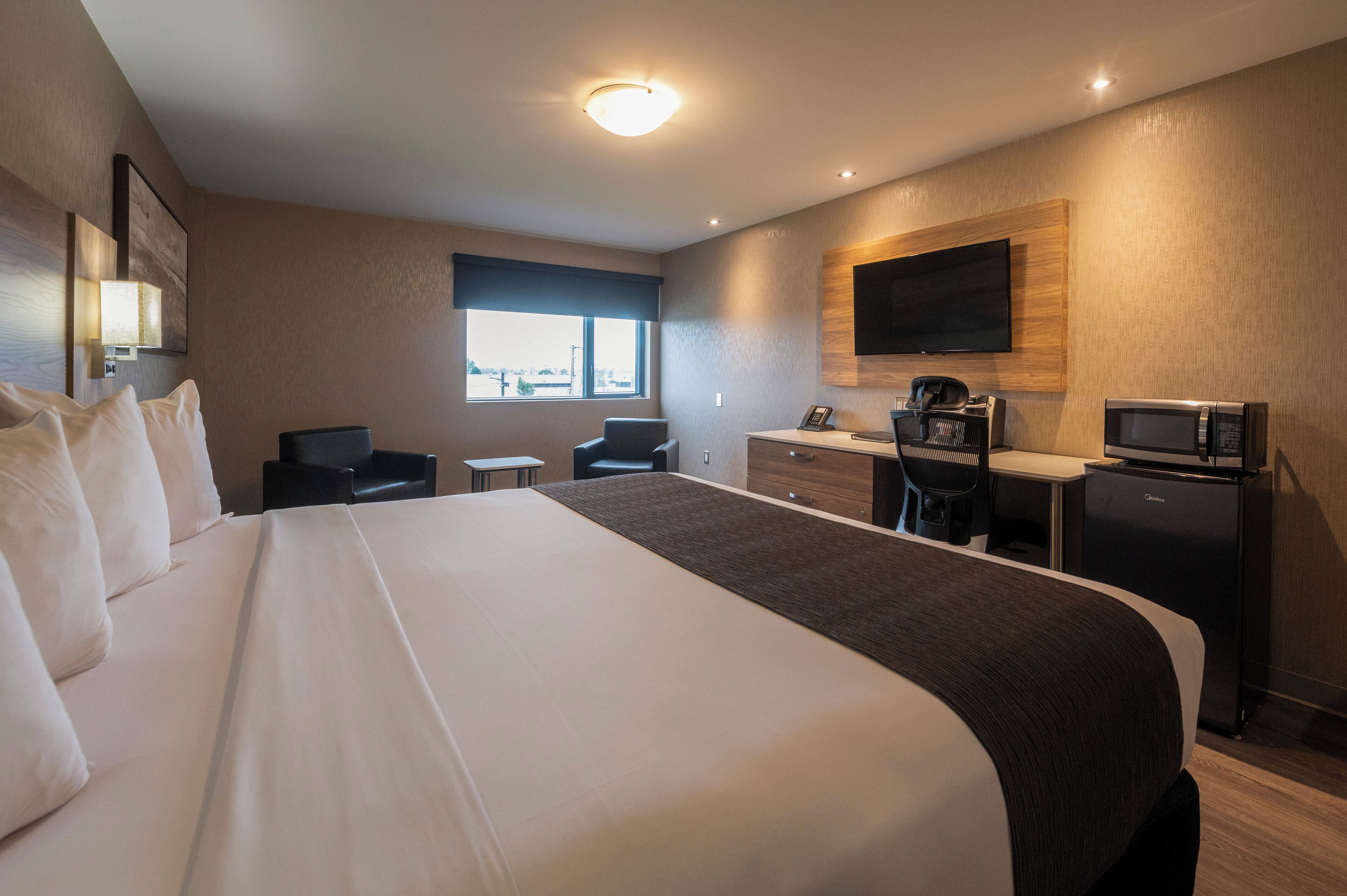 Habitación de hotel con una cama grande, un escritorio con silla, un microondas y un televisor en la pared.