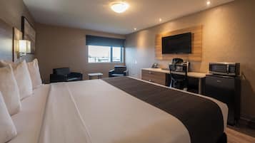 Habitación de hotel con una cama grande, un escritorio con silla, un microondas y un televisor en la pared.