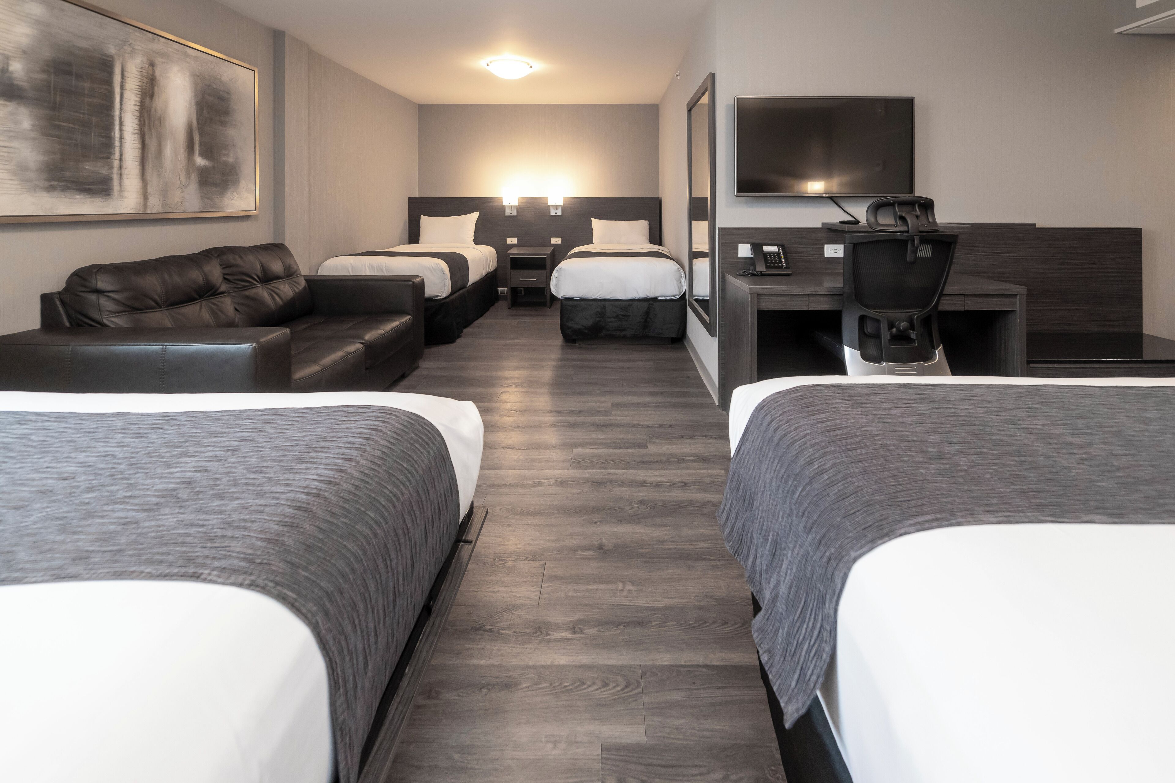 A hotel room with two beds, a sofa, a desk, and a TV.