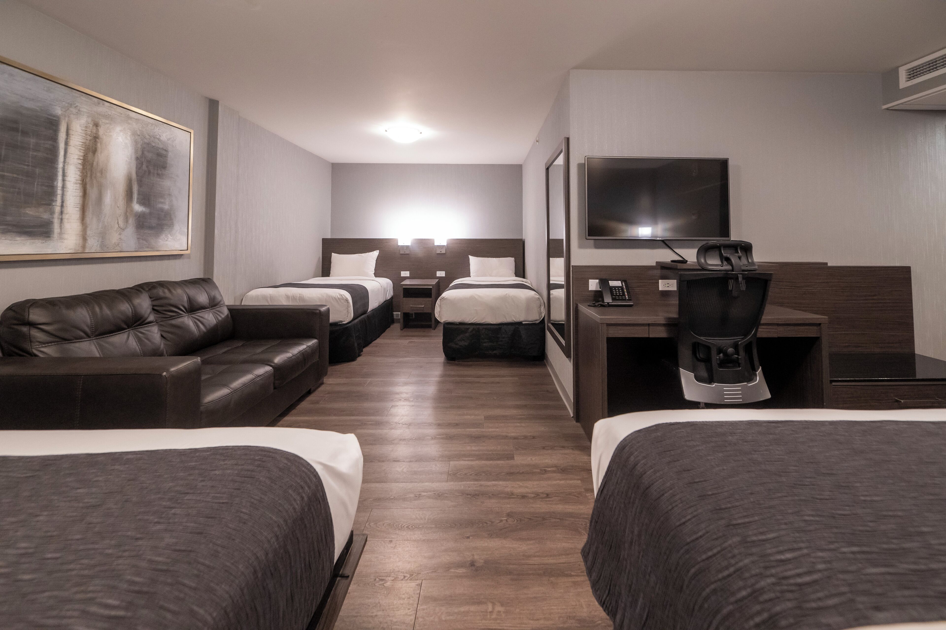 A hotel room with two beds, a sofa, a desk, a TV, and a coffee maker.