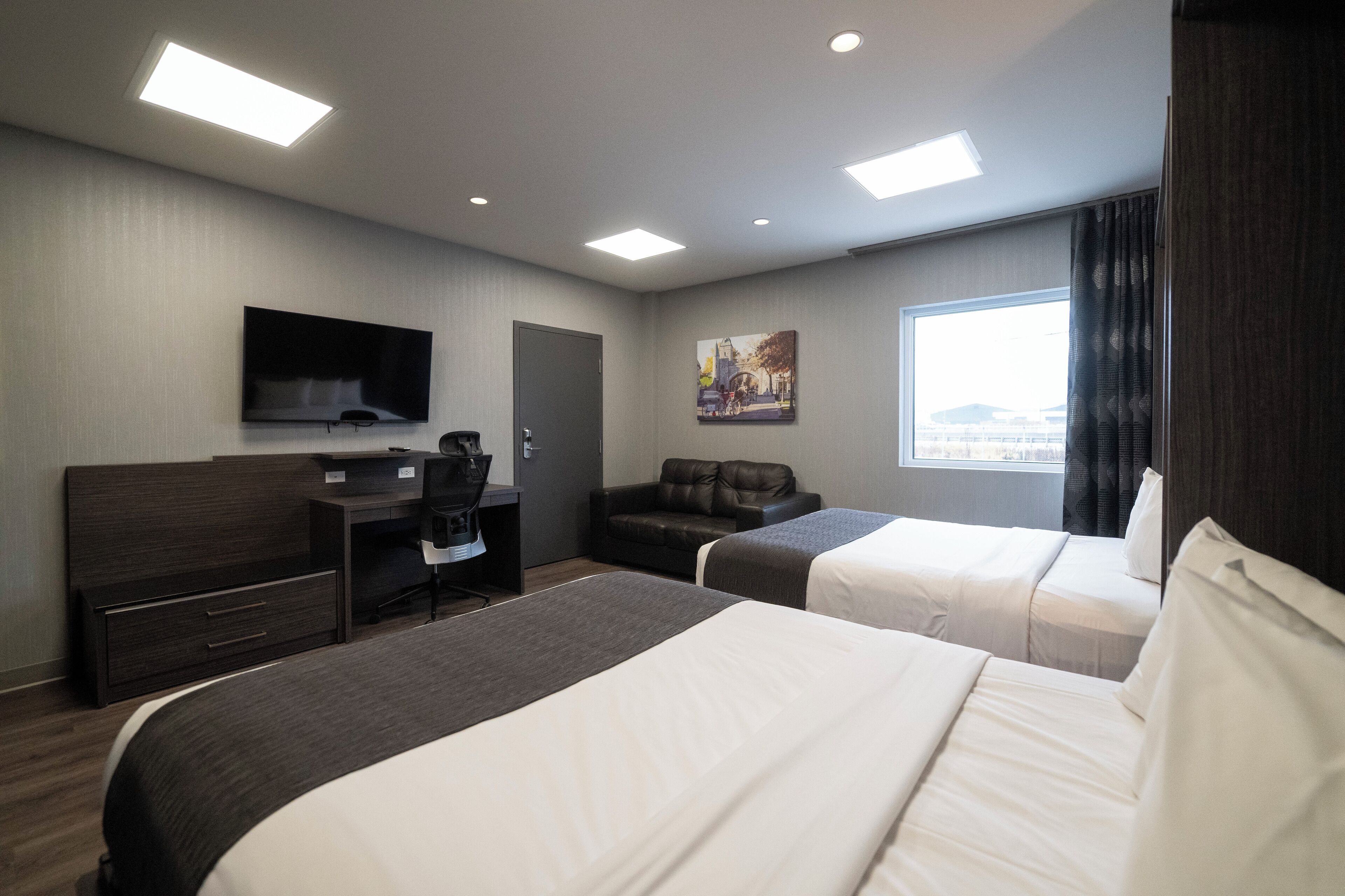 A hotel room with two beds, a desk, a chair, a TV, and a window with a city view.