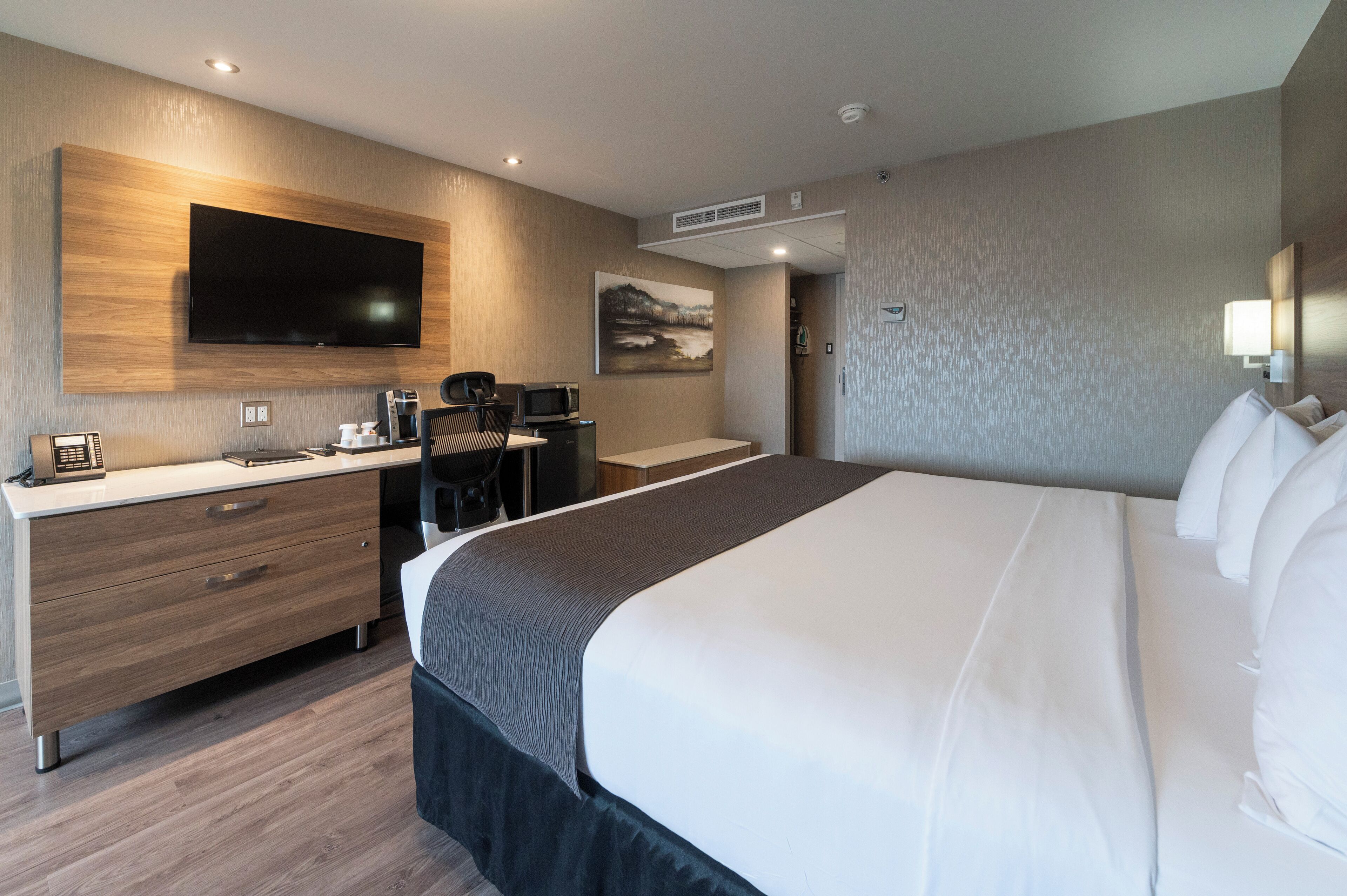 Une chambre d’hôtel moderne dotée d’un grand lit, d’un téléviseur à écran plat fixé au mur, d’un bureau avec une chaise et d’une machine à café.
