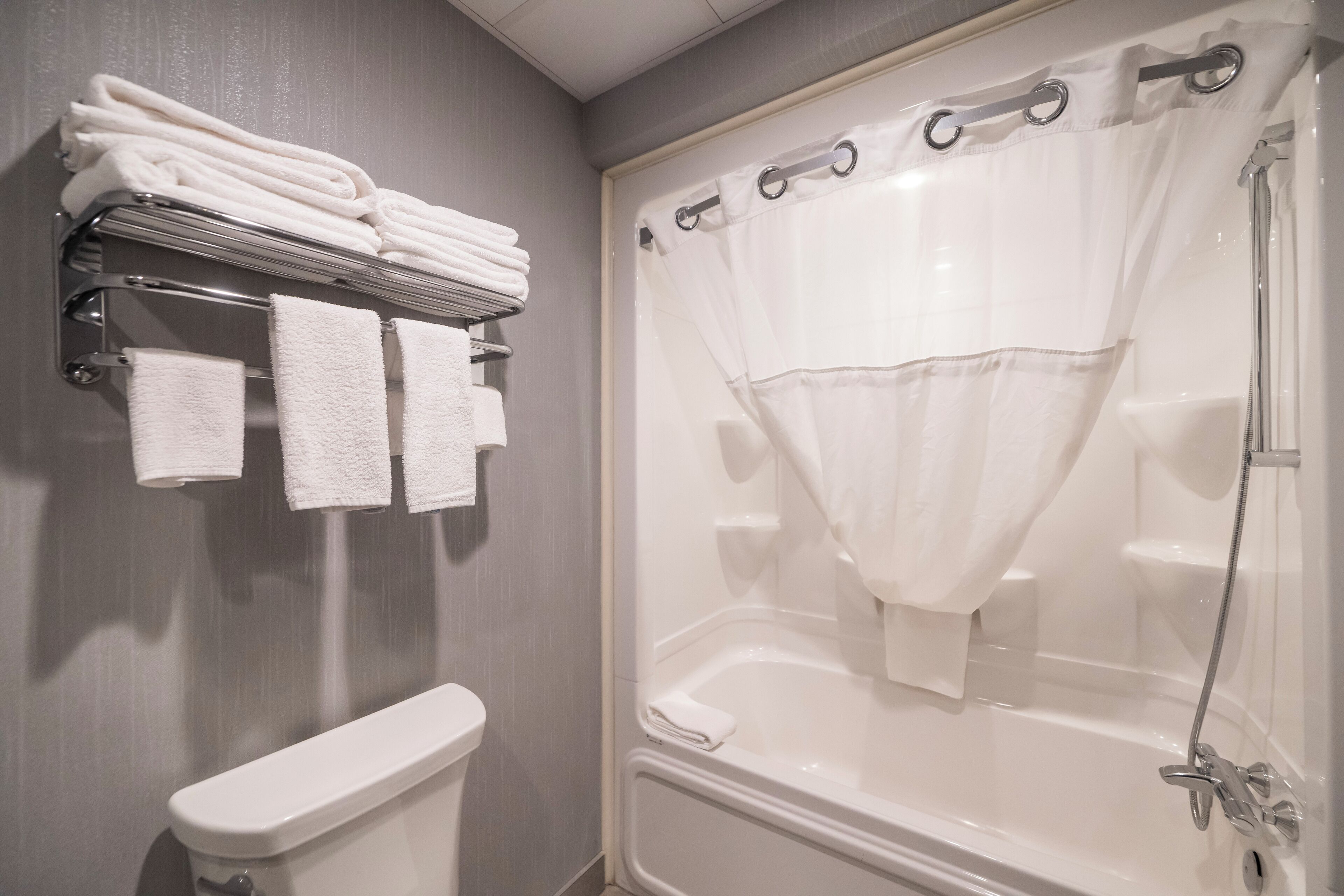 Une salle de bain comprenant des toilettes, une baignoire avec un rideau de douche et un porte-serviettes avec des serviettes pliées.