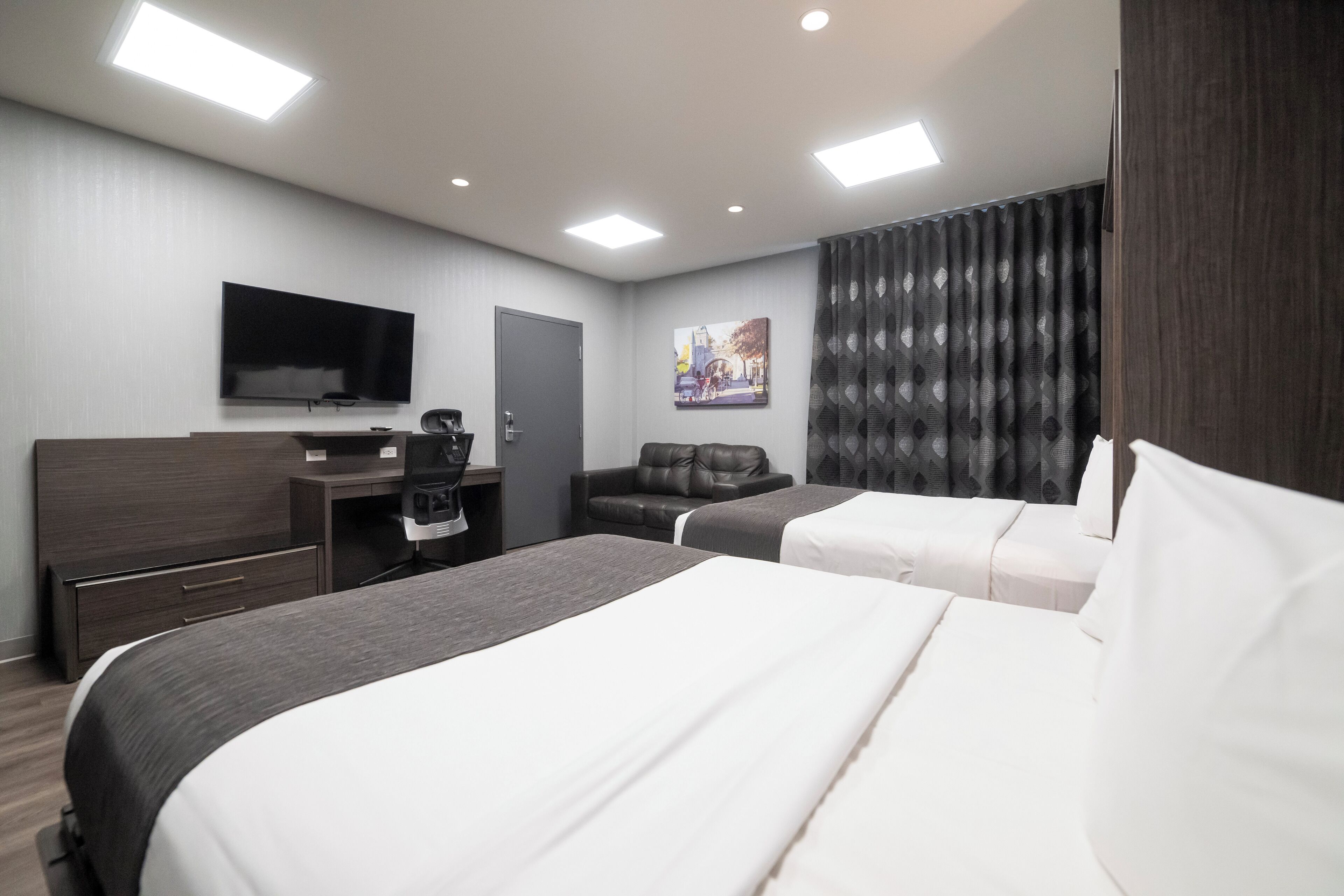 A modern hotel room with a large bed, a desk, a chair, a flat-screen TV, and a painting on the wall.