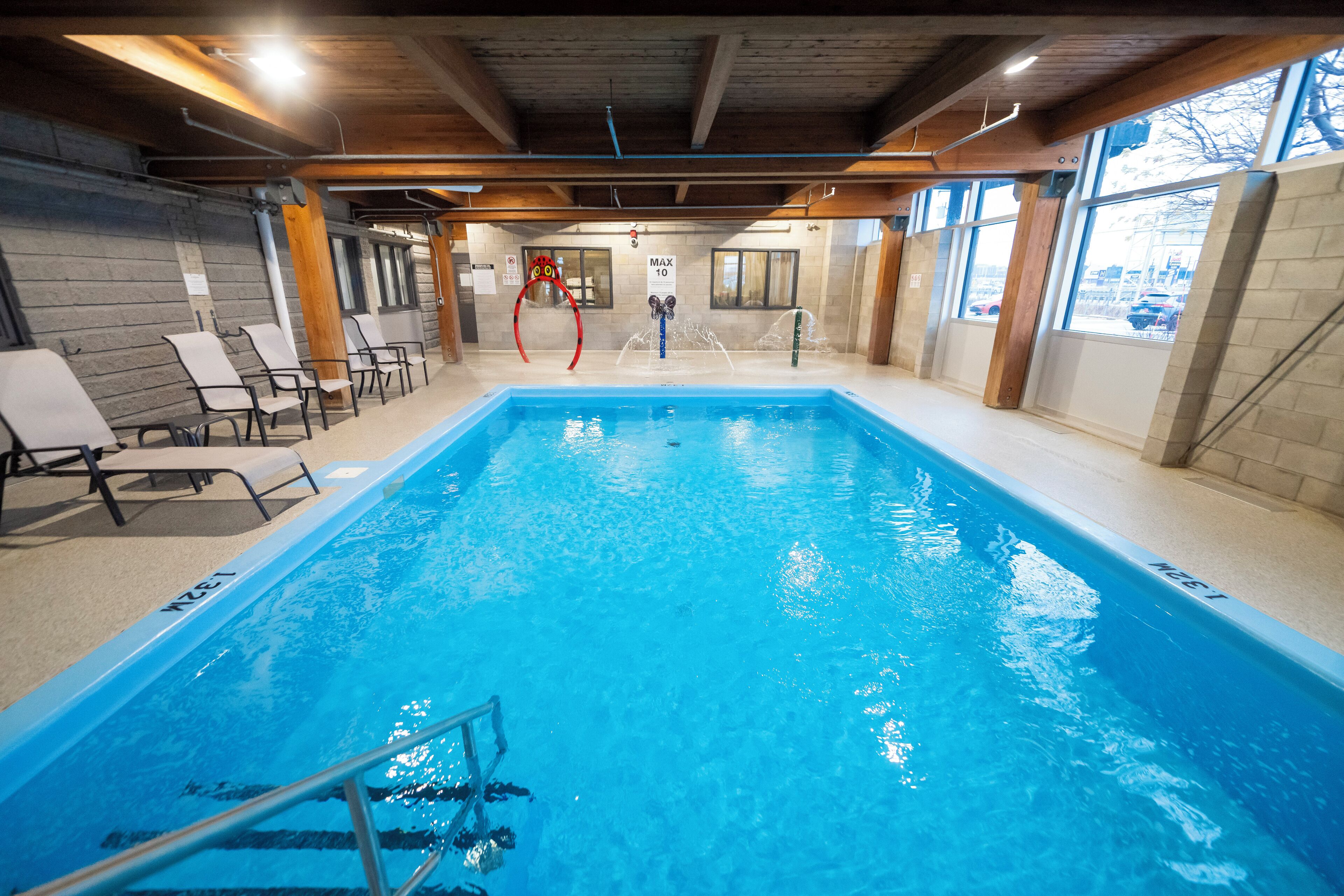 An indoor swimming pool with clear blue water, wooden beams on the ceiling, and lounge chairs along the side.