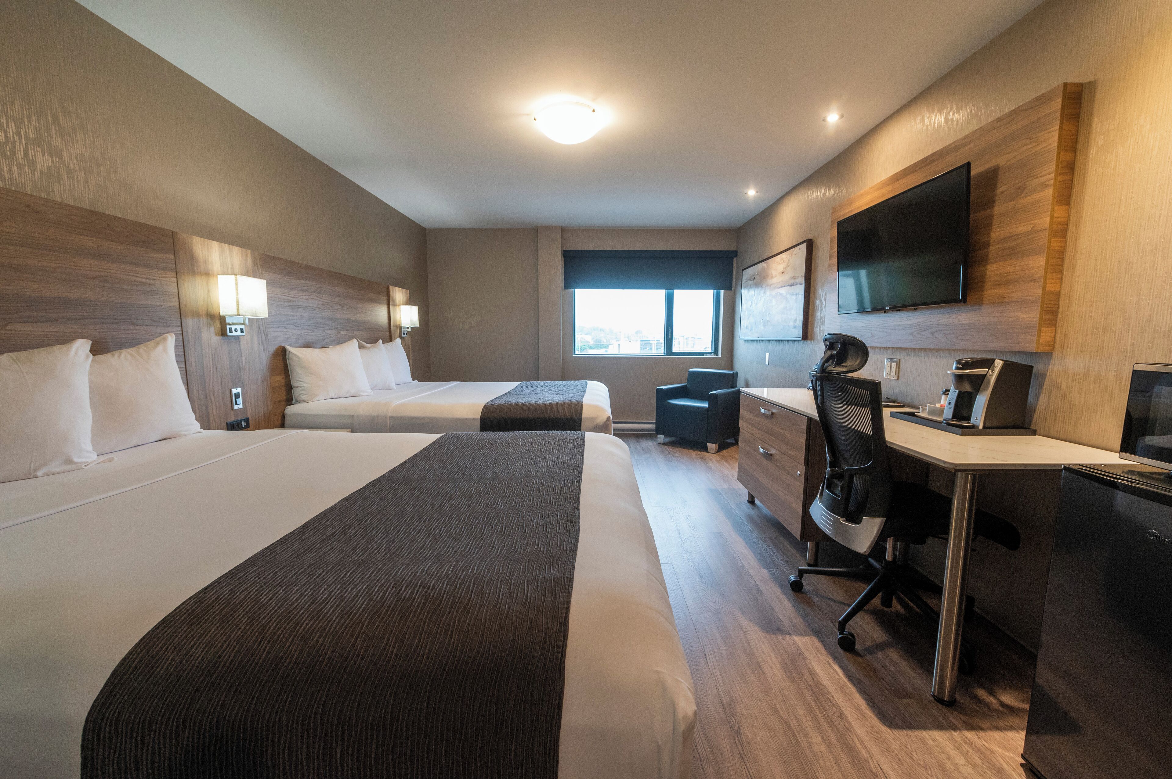 Ein Hotelzimmer mit zwei Betten, einem Schreibtisch, einem Sessel, einem Fernseher und einem Fenster.