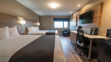 Ein Hotelzimmer mit zwei Betten, einem Schreibtisch, einem Sessel, einem Fernseher und einem Fenster.