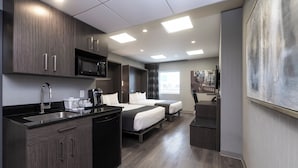 Una habitación de hotel moderna con kitchenette, dos camas, un ventanal grande y un cuadro en la pared.