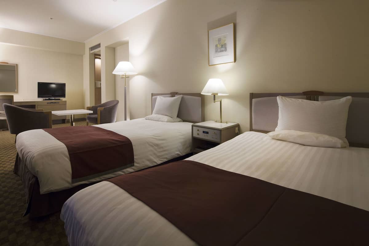 Een hotelkamer met twee bedden, een bureau, een stoel en een televisie.